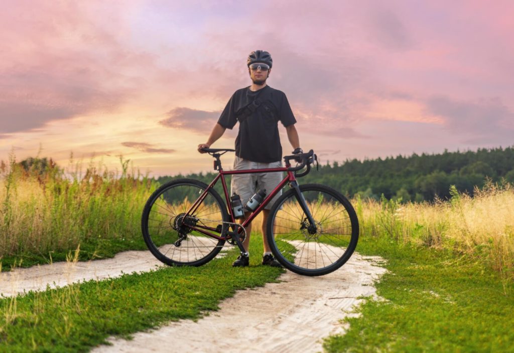 male cyclist stands behind his gravel bike